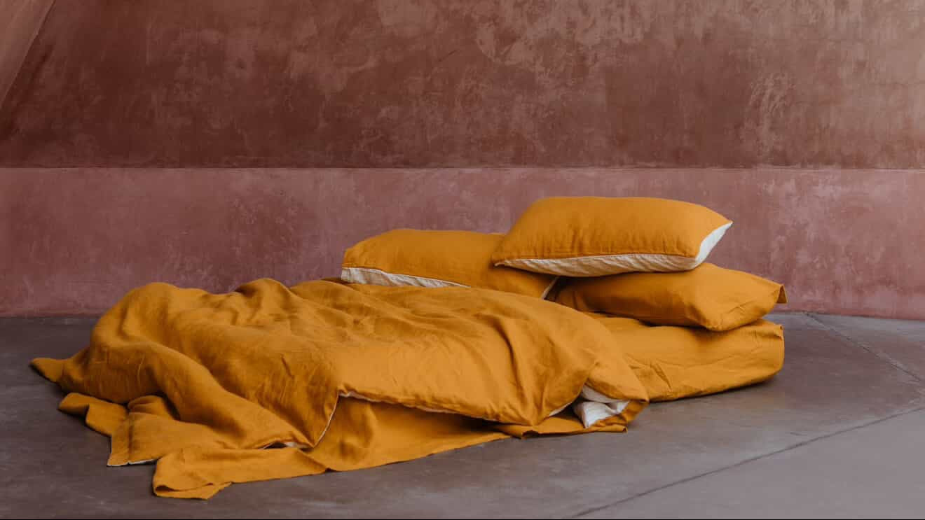 Mustard bedding and pillows on a bed against a textured pink wall.