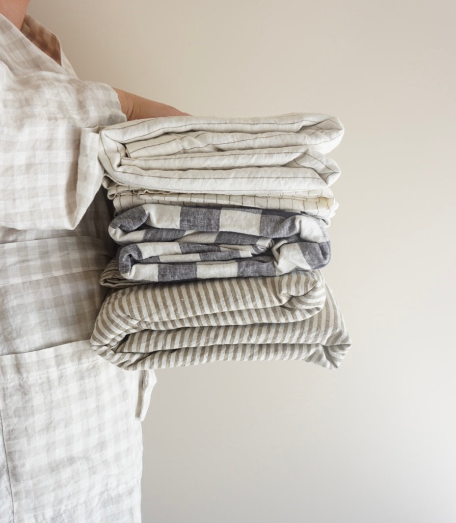 Simple Linen Co, Model wearing Dove Grey Gingham dressing gown, holding 3 Simple Linen Co Duvet Covers neatly folded
