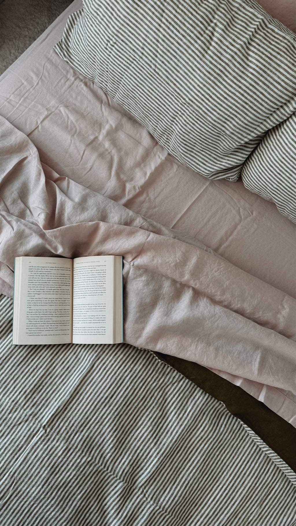 Simple Linen Co. 100% French flax linen sheet set in Light pink, featured with Liv, Olive and Olive Stripe double sided duvet cover set, top down view of bed with an open book.