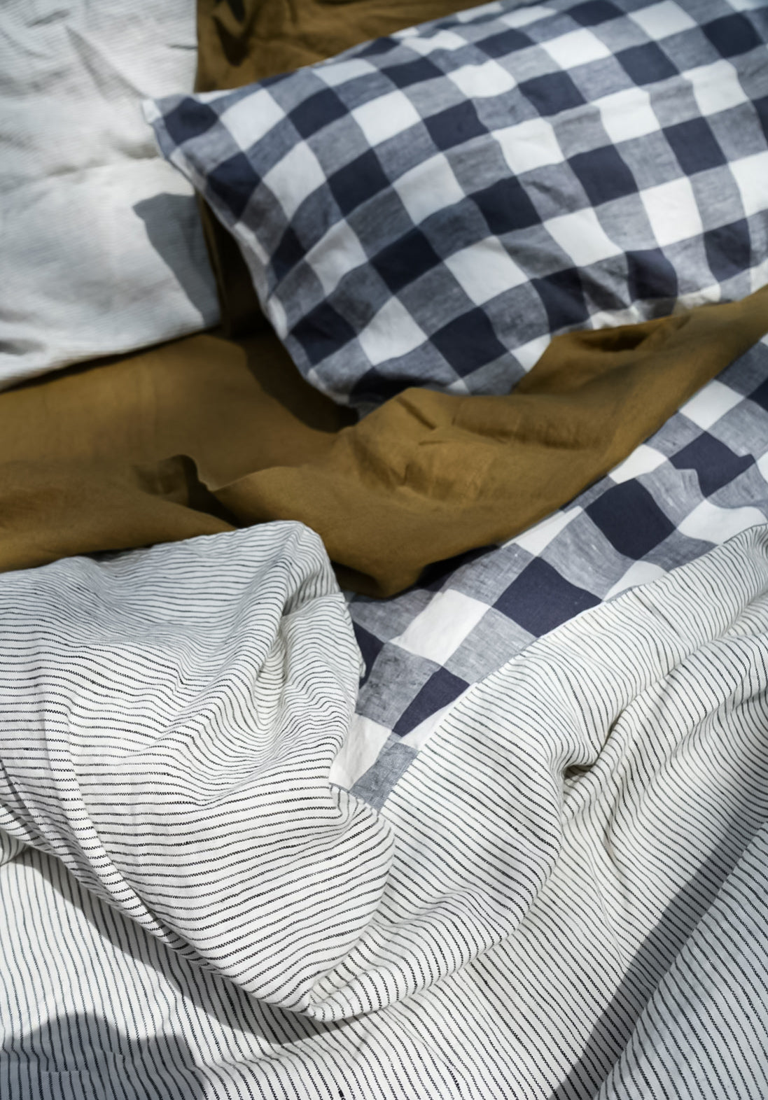 Simple Linen Co. 100% French flax linen sheet set in Olive, featured with double sided duvet cover set Romy in Pinstripe and Night Blue Grids, top down, messy bed view.