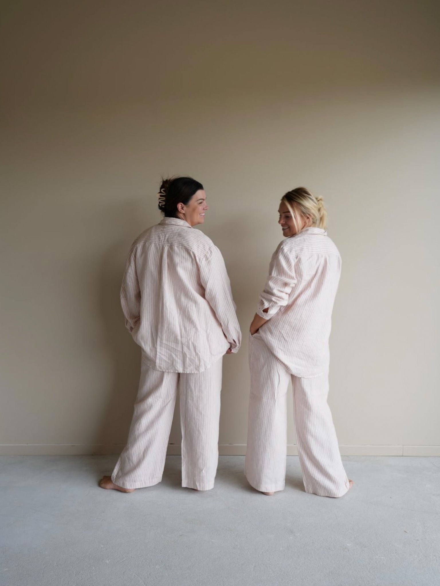 Back view of Simple Linen Co’s long sleeve day to night wear set in pink stripe, two models showcasing both universal sizes, made from 100% French Flax Linen. 