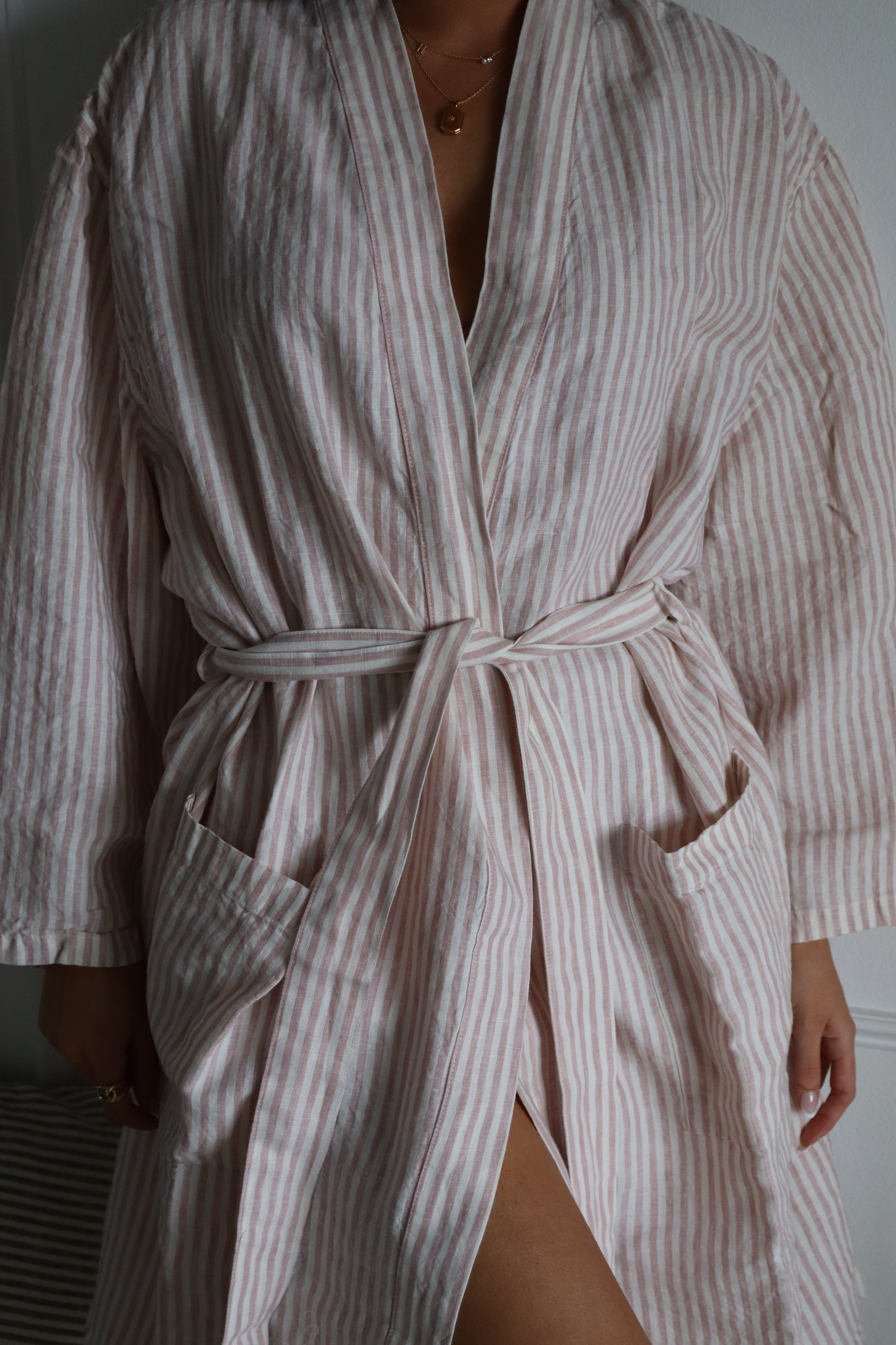 A woman wearing simple linen co's pink stripe dressing gown, only her body is visible.